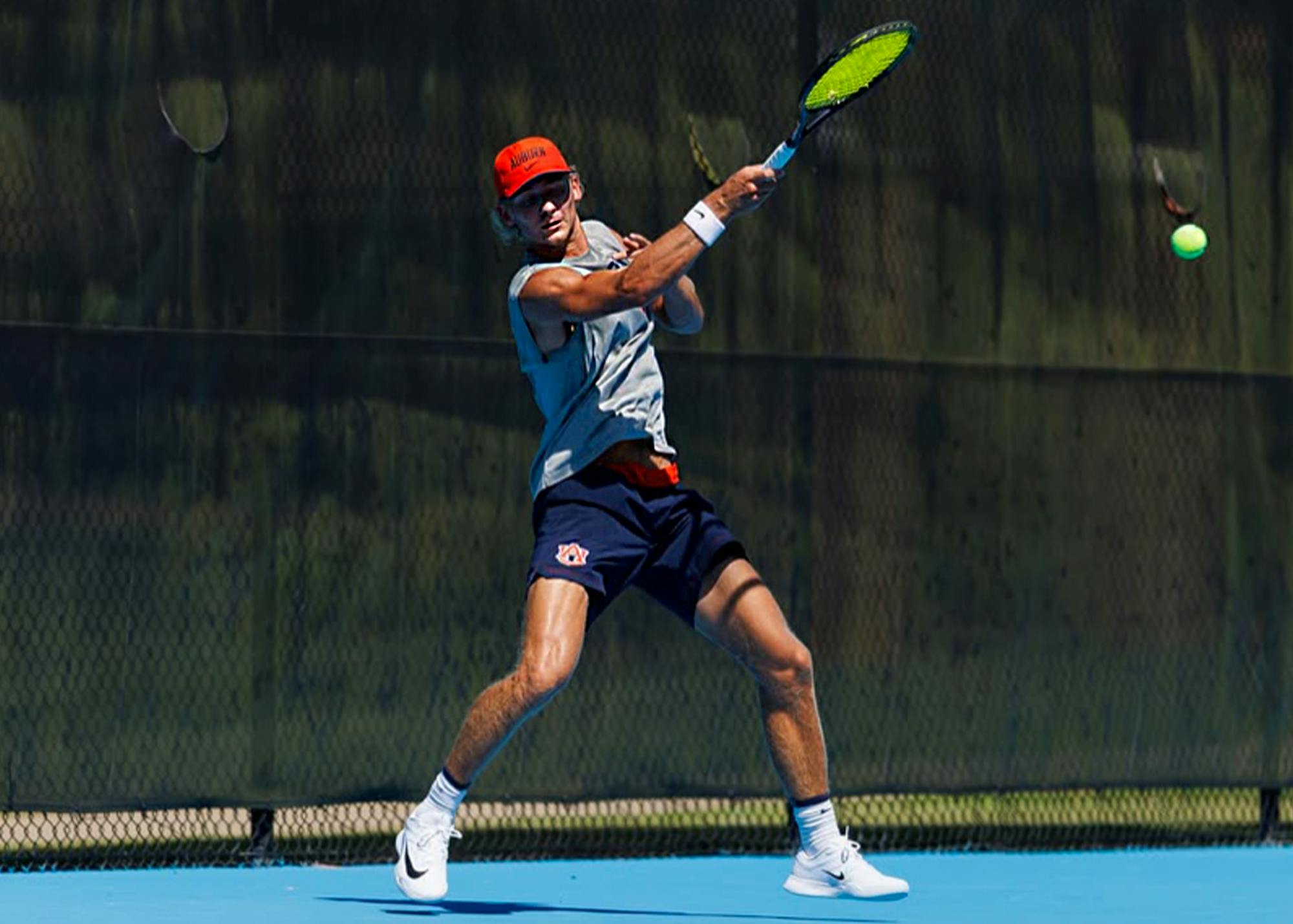 Auburn men’s tennis player Duje Markovina hits a forehand during a match on a blue tennis court.