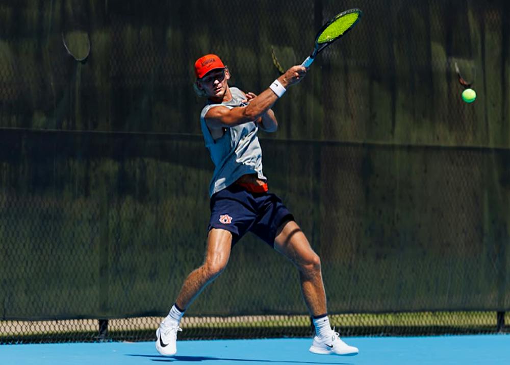 Auburn men’s tennis player Duje Markovina hits a forehand during a match on a blue tennis court.