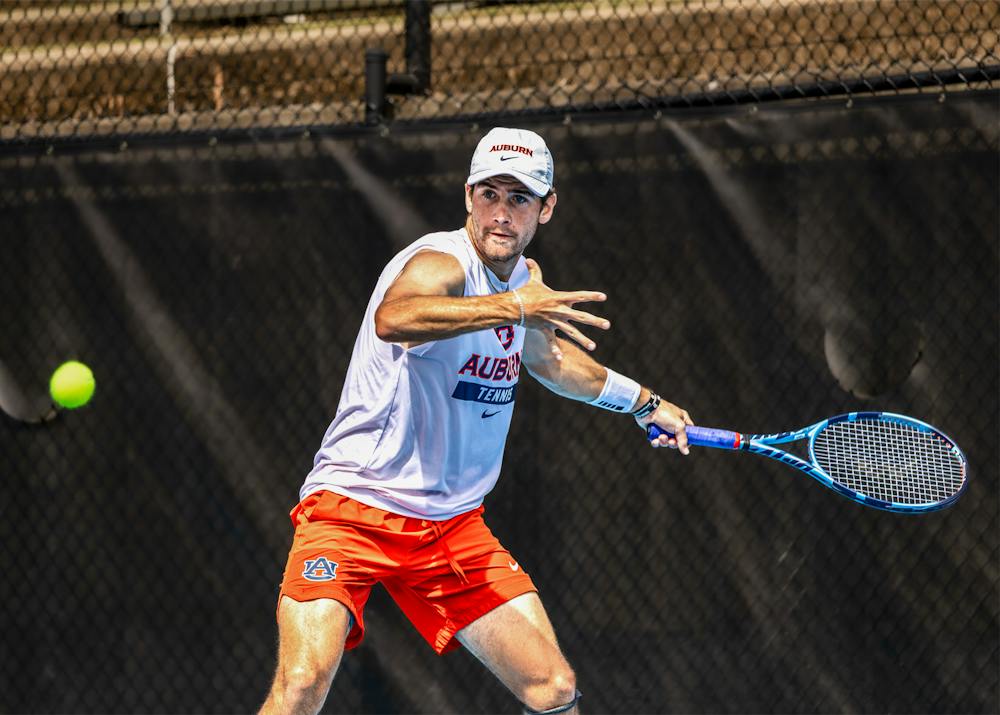 Auburn men’s tennis player Joey Phillips prepares to hit a tennis ball during a match, wearing an Auburn tennis shirt, orange shorts and a white Auburn cap.