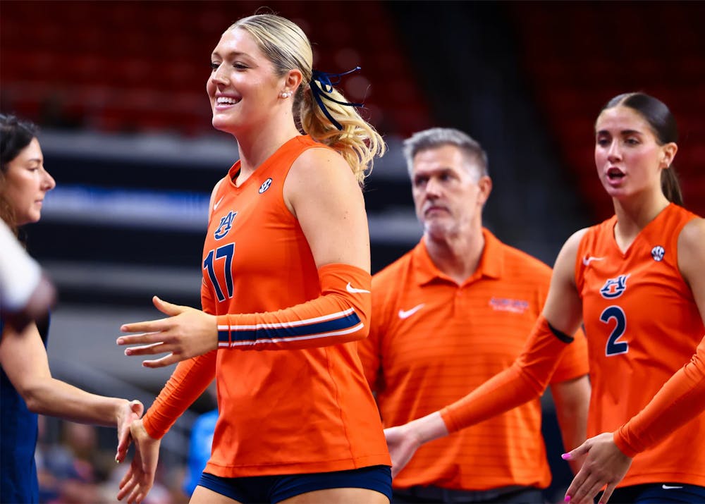 Auburn volleyball player Grace Havlicek, wearing No. 17, smiles and reaches out to high-five a teammate during a match. Teammate No. 2 and an Auburn coach are visible in the background.