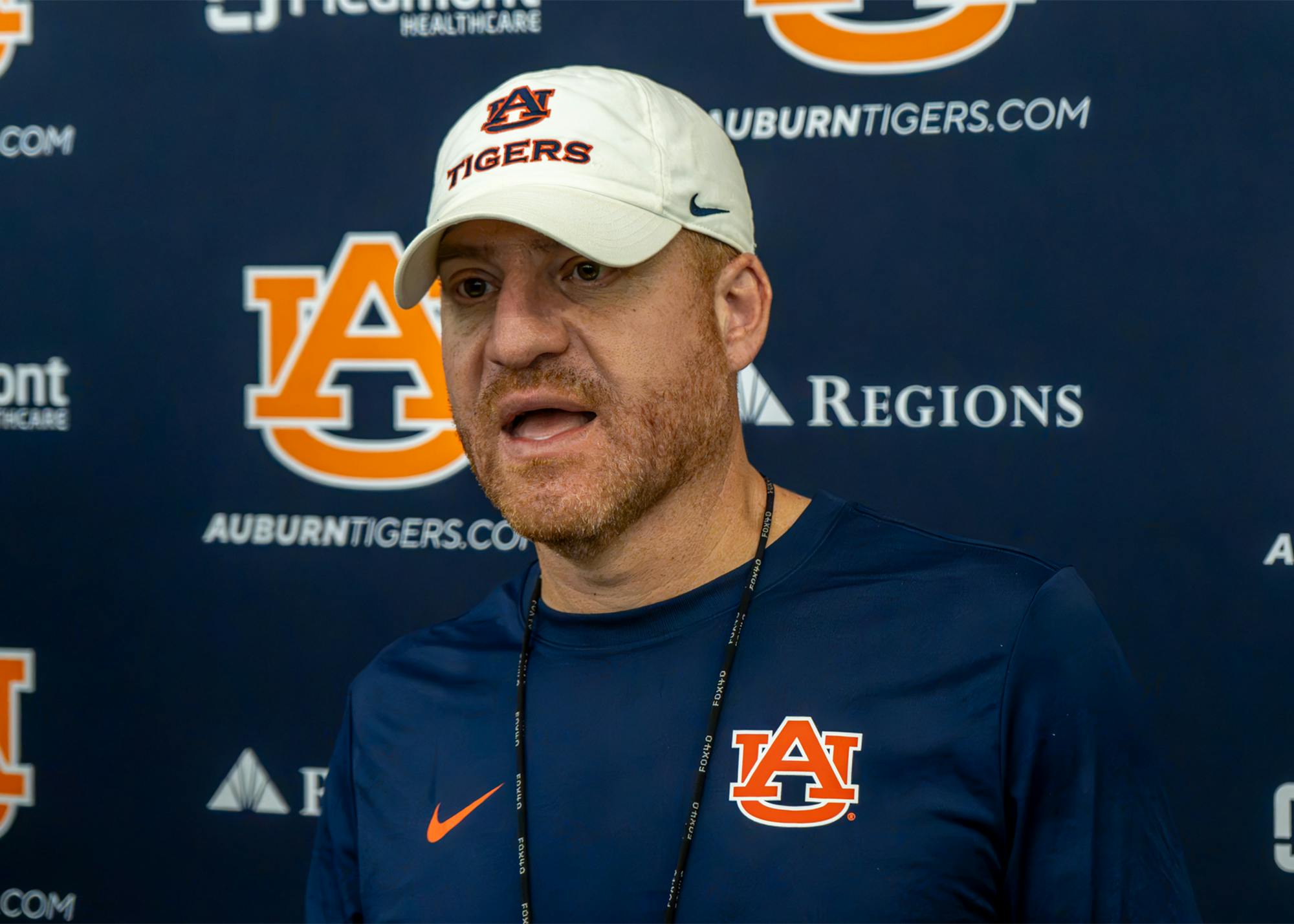 Auburn head football coach Alex Golesh speaks during a press conference while wearing an Auburn cap and navy Auburn shirt.