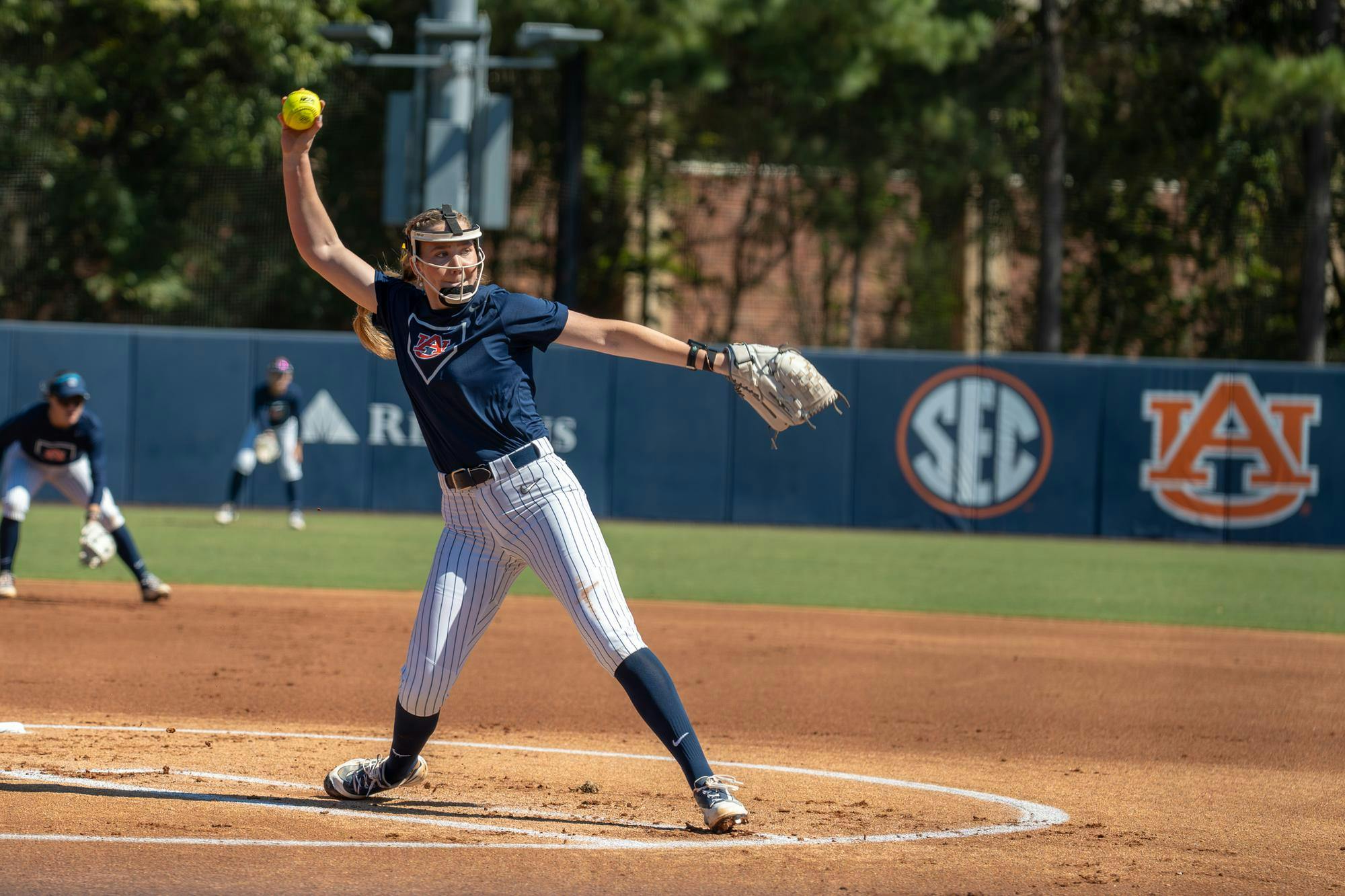 Auburn softball pitcher delivers a pitch during a game, with teammates positioned behind her on the field.