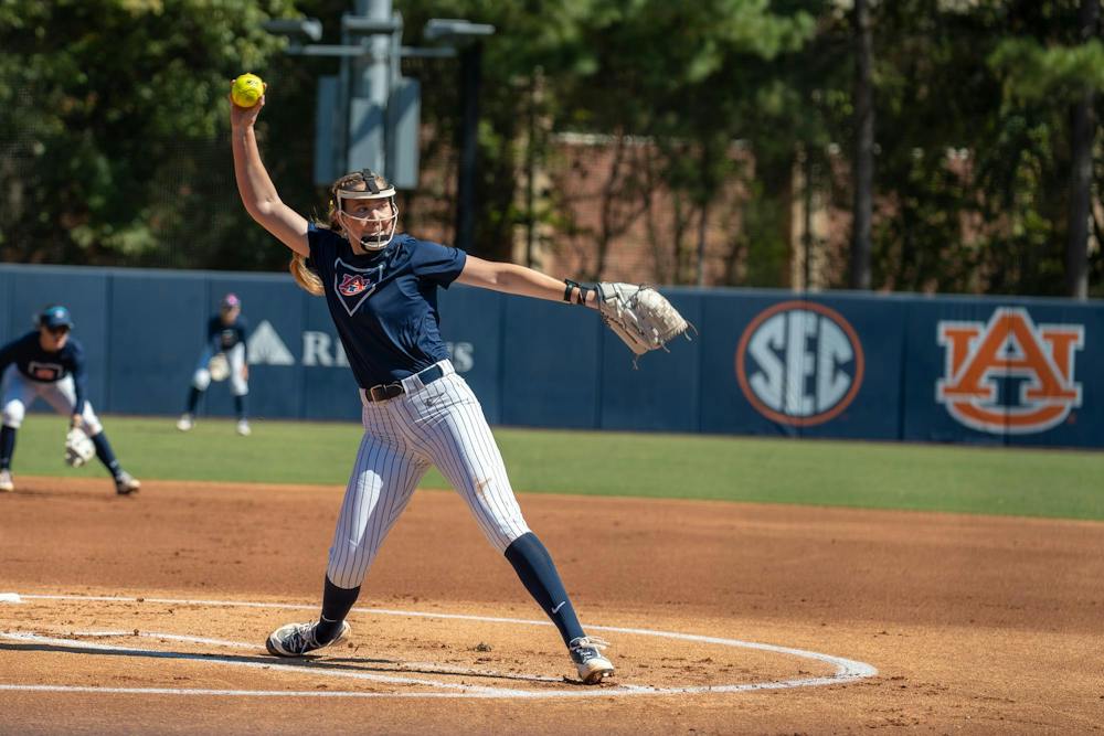 Auburn softball pitcher delivers a pitch during a game, with teammates positioned behind her on the field.