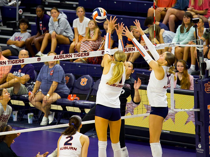 Two Auburn Volleyball players, Kate Mansfield and Bel Zimmerman, jump together in front of the net to attempt a block against Mississippi State. They are wearing white uniforms.