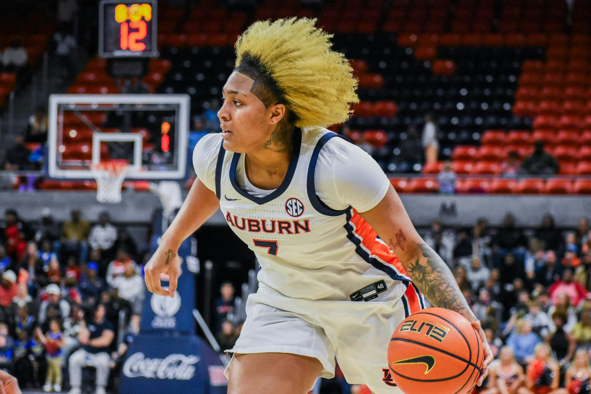 A player in a white Auburn jersey dribbles a basketball while moving swiftly on a court, with spectators in the background.