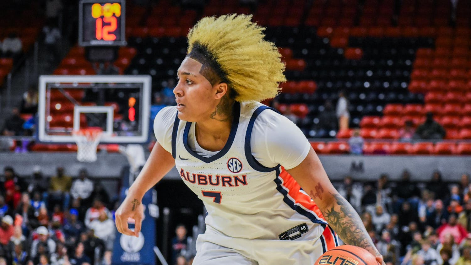 A player in a white Auburn jersey dribbles a basketball while moving swiftly on a court, with spectators in the background.