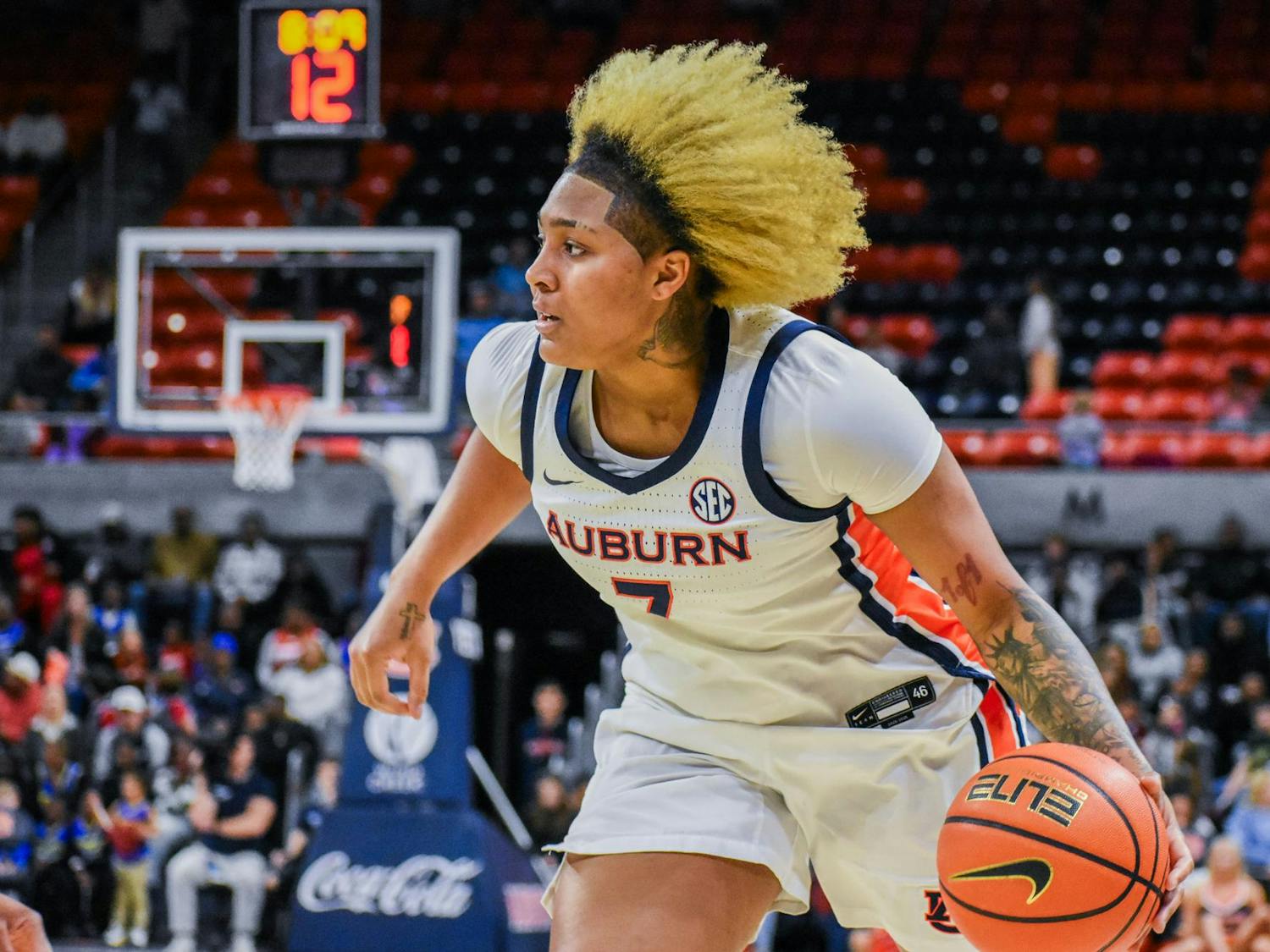 A player in a white Auburn jersey dribbles a basketball while moving swiftly on a court, with spectators in the background.
