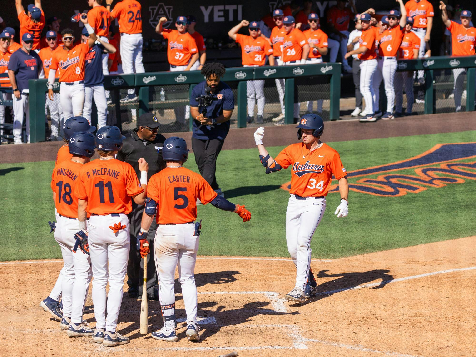 A group of baseball players in orange jerseys celebrates at home plate while an umpire discusses something with them.