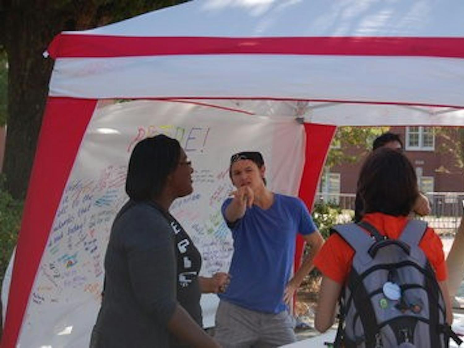 Braxton Tanner, sophomore in zoology and director of political affairs with AGSA, dances on the concourse Monday as passing students sign messages of love on National Coming Out Day. (Brian Woodham / Associate Copy Editor)