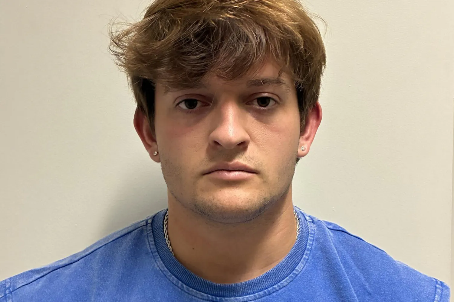 A young man with short, wavy brown hair and a blue sleeveless shirt stares directly at the camera against a plain background. Zane Hanson Lynch, 22, of Auburn.