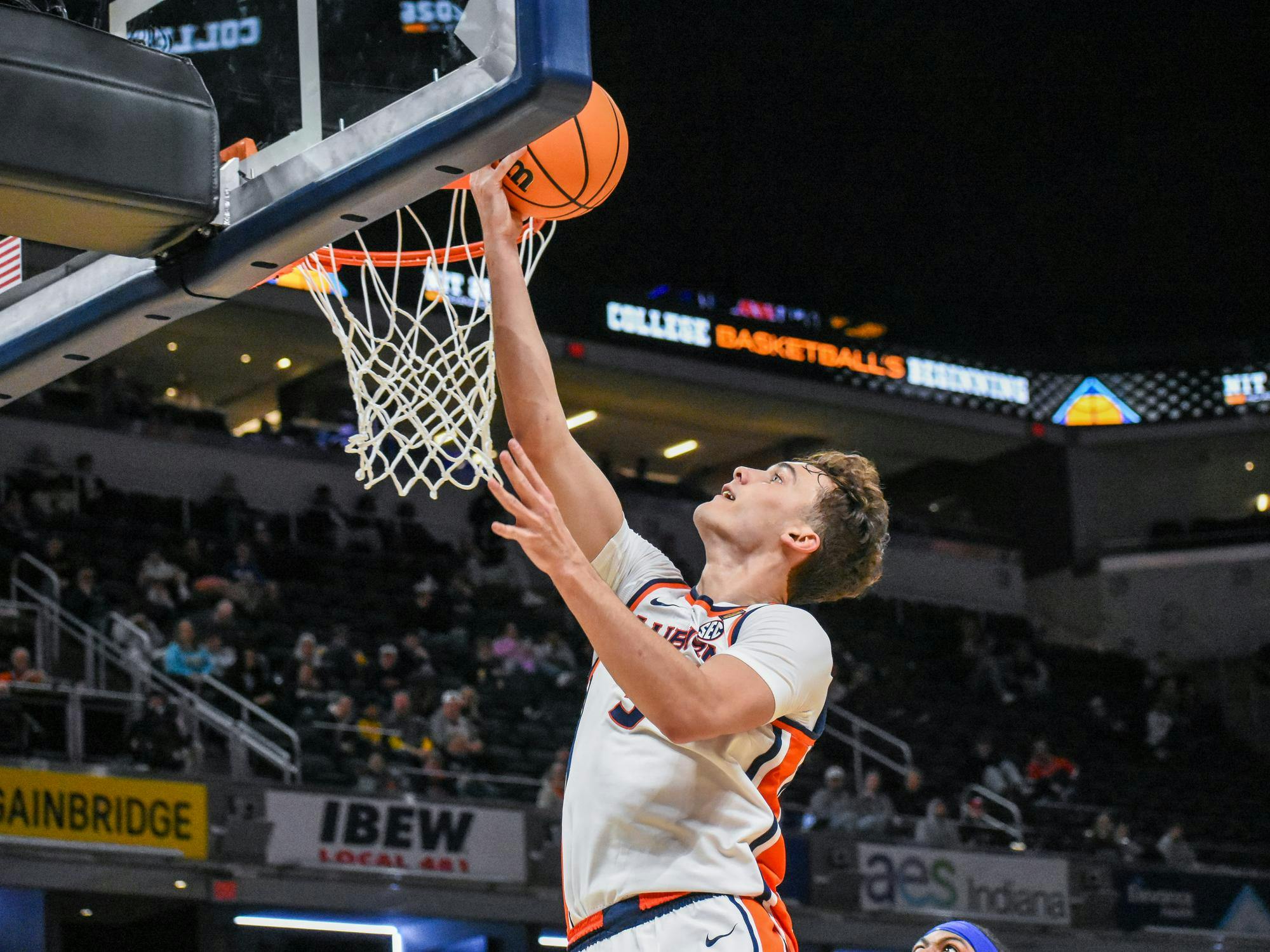 A player leaps towards the basketball hoop, reaching to score while another player watches from below.