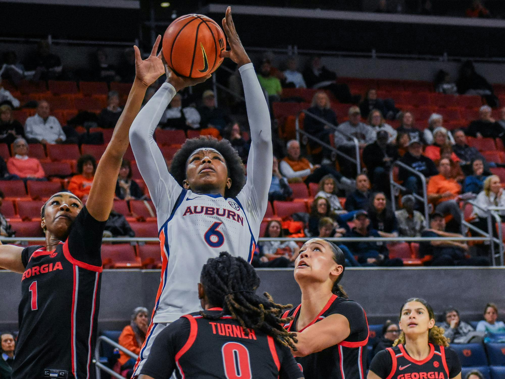 A player in an Auburn jersey jumps to shoot a basketball while surrounded by defenders wearing Georgia jerseys.