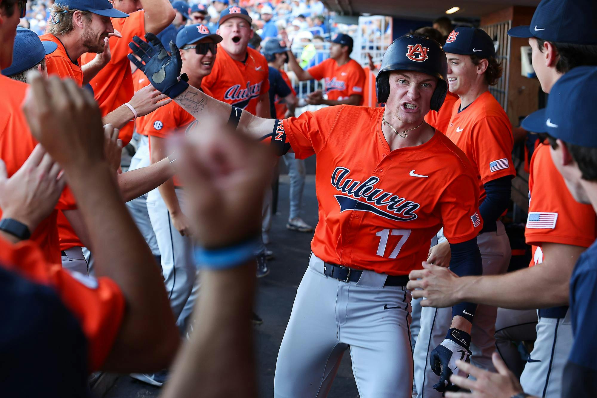 A group of excited baseball players in orange jerseys celebrate in a dugout, high-fiving and cheering.