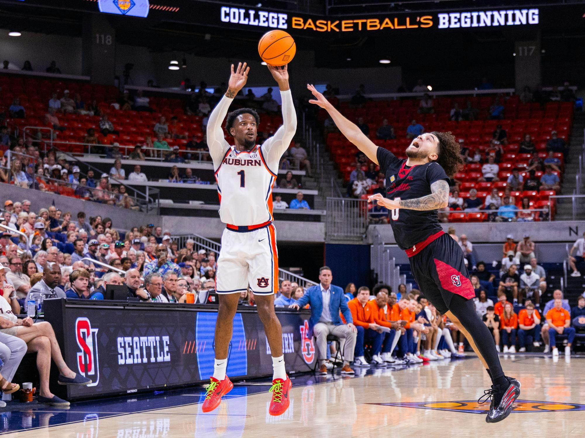 A basketball player from Auburn jumps to shoot while a defender from Seattle attempts to block the shot, with a crowd watching.