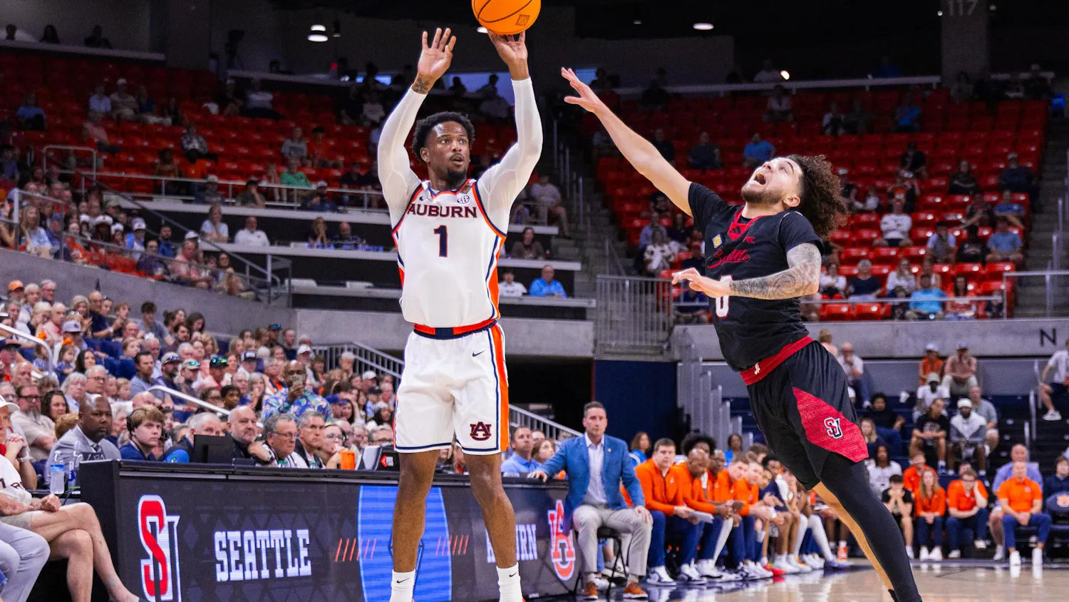 A basketball player from Auburn jumps to shoot while a defender from Seattle attempts to block the shot, with a crowd watching.