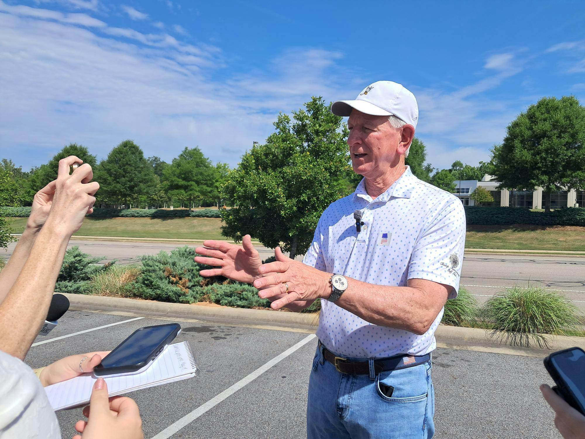 Sen. Tommy Tuberville speaks at a press conference in Auburn on May 19. He is wearing a white baseball cap, a wristwatch and a Trump International Golf Club polo with an “I voted” sticker.