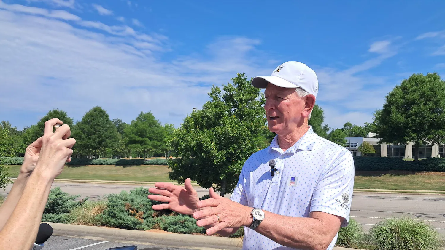 Sen. Tommy Tuberville speaks at a press conference in Auburn on May 19. He is wearing a white baseball cap, a wristwatch and a Trump International Golf Club polo with an “I voted” sticker.