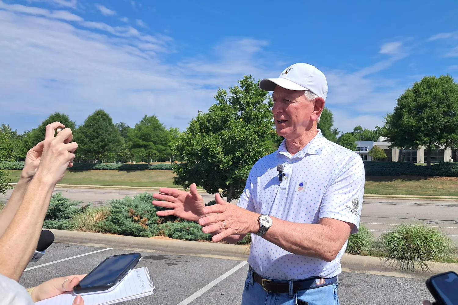 Sen. Tommy Tuberville speaks at a press conference in Auburn on May 19. He is wearing a white baseball cap, a wristwatch and a Trump International Golf Club polo with an “I voted” sticker.