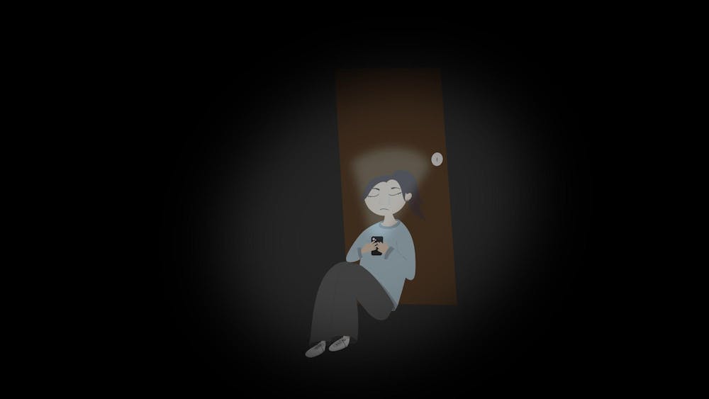 <p>A person sits against a door in a dimly lit space, looking at their phone with a scared expression.</p>
