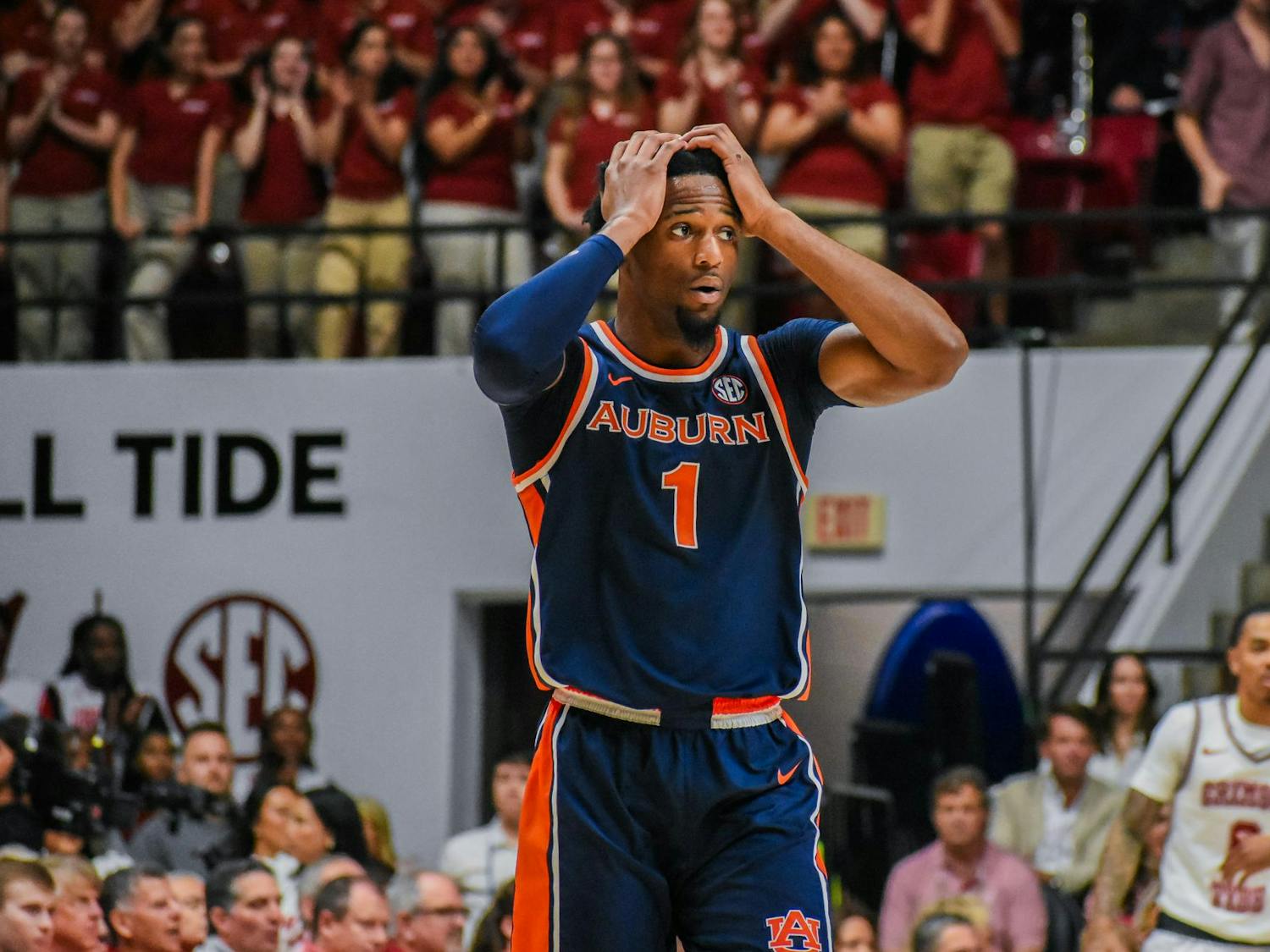A player in an Auburn basketball uniform looks distressed, while a crowd in the background shows excitement.