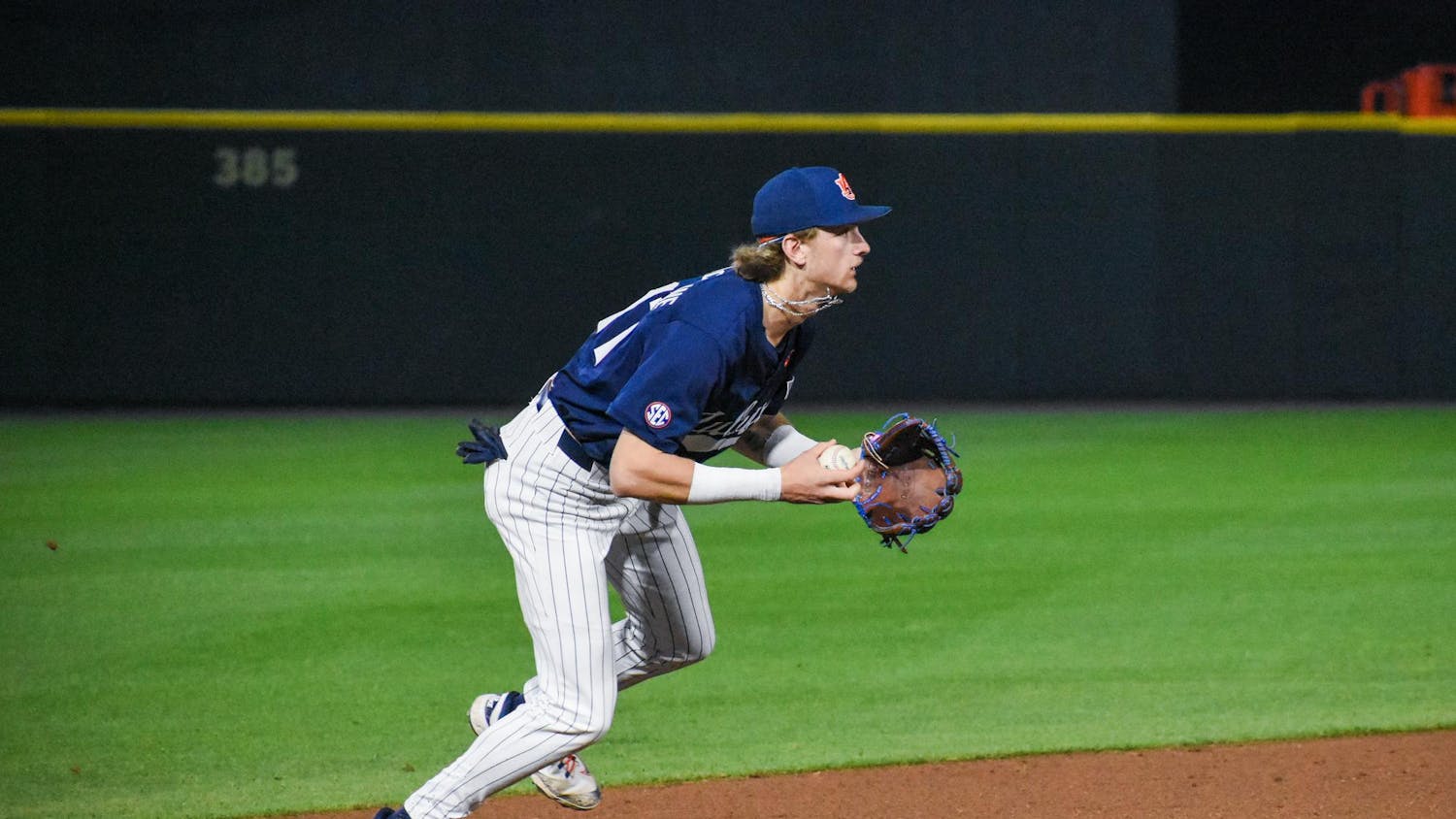 A baseball player in a navy jersey and striped pants is crouching on an infield, preparing to field a ball.