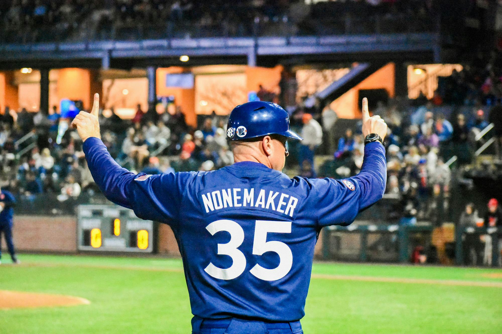 A man in a blue baseball jersey with the name "NONEMAKER" and the number "35" raises his hand while facing a crowd.