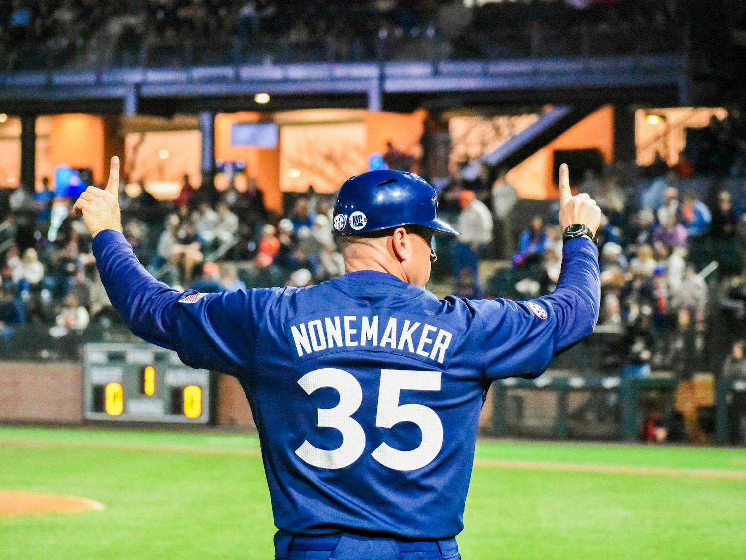 A man in a blue baseball jersey with the name "NONEMAKER" and the number "35" raises his hand while facing a crowd.
