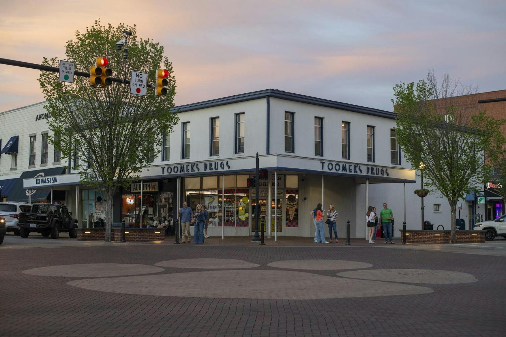 A two-story building labeled "Toomey's Drugs" sits on a corner, with people gathered nearby, under a sunset sky.
