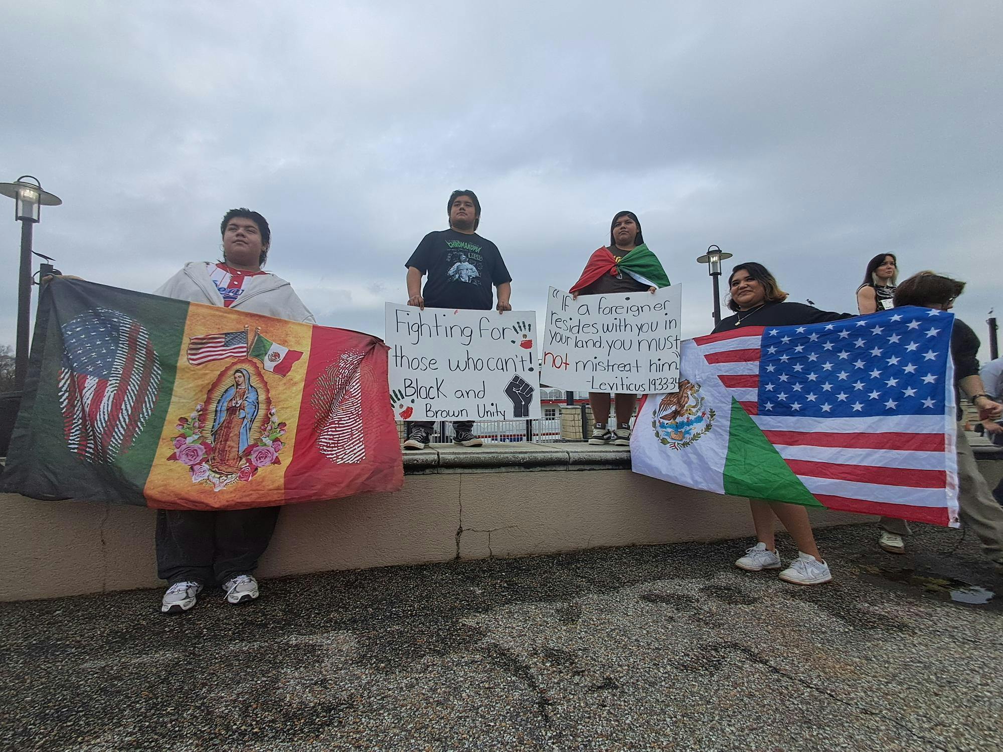 Protesters hold Mexican and American flags alongside protest signs about unity and Leviticus 19:33-34.
