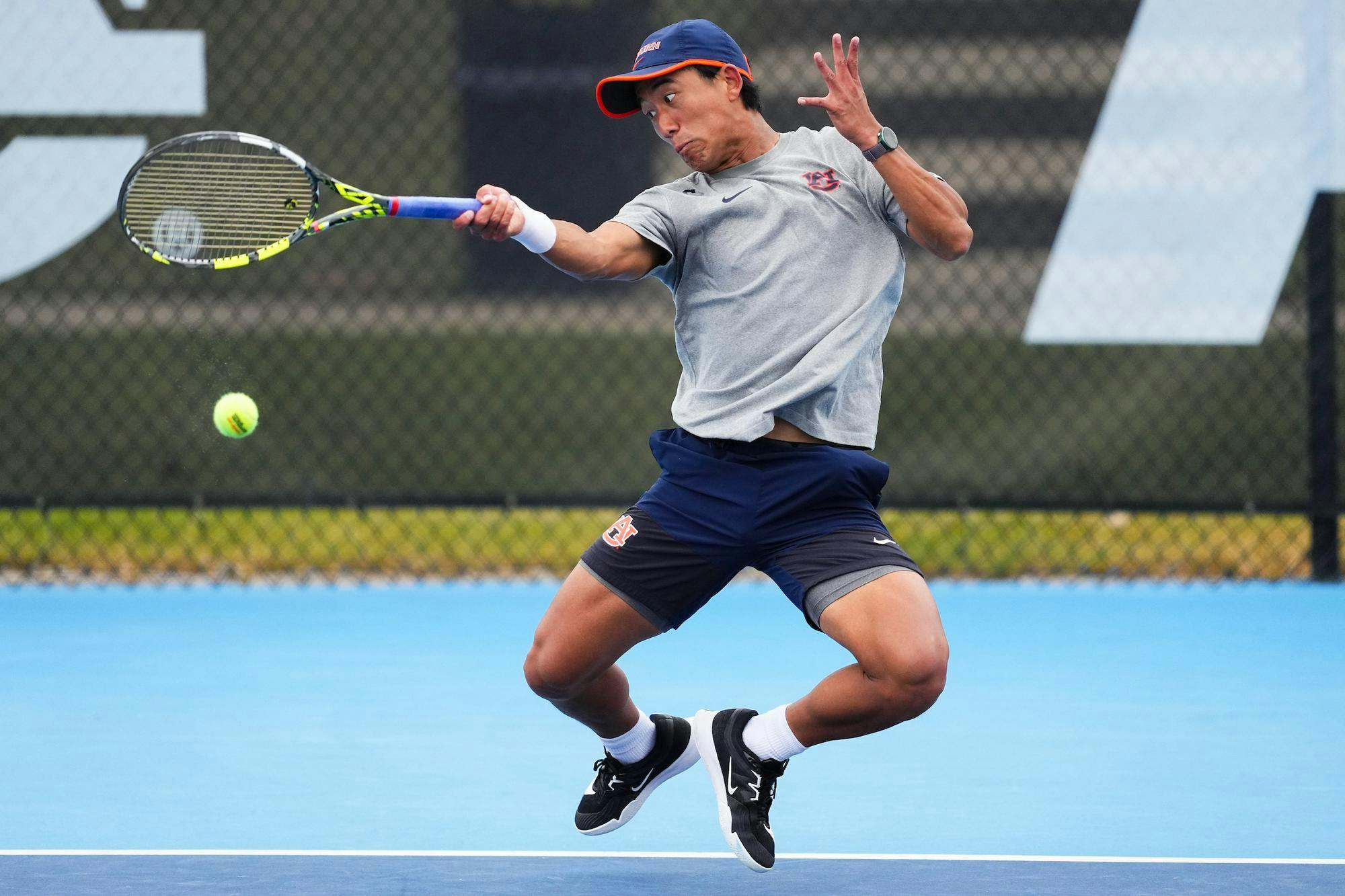 A tennis player in motion, striking a ball while wearing a gray shirt, blue shorts, and black shoes.