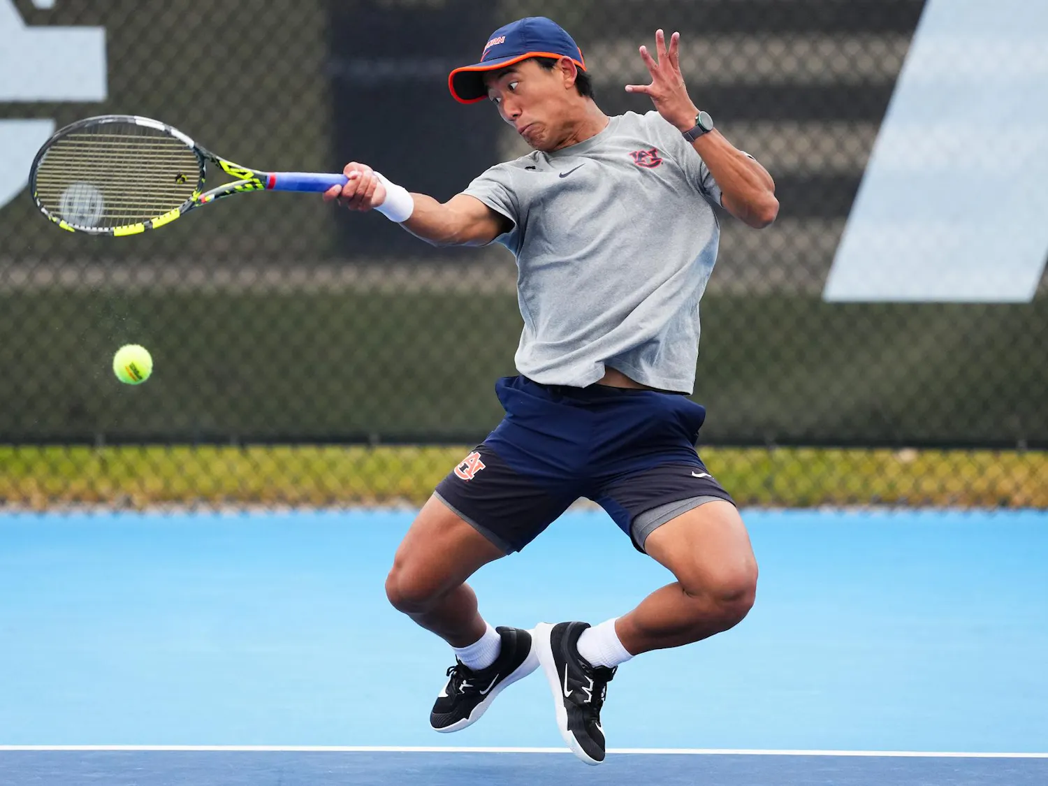 A tennis player in motion, striking a ball while wearing a gray shirt, blue shorts, and black shoes.