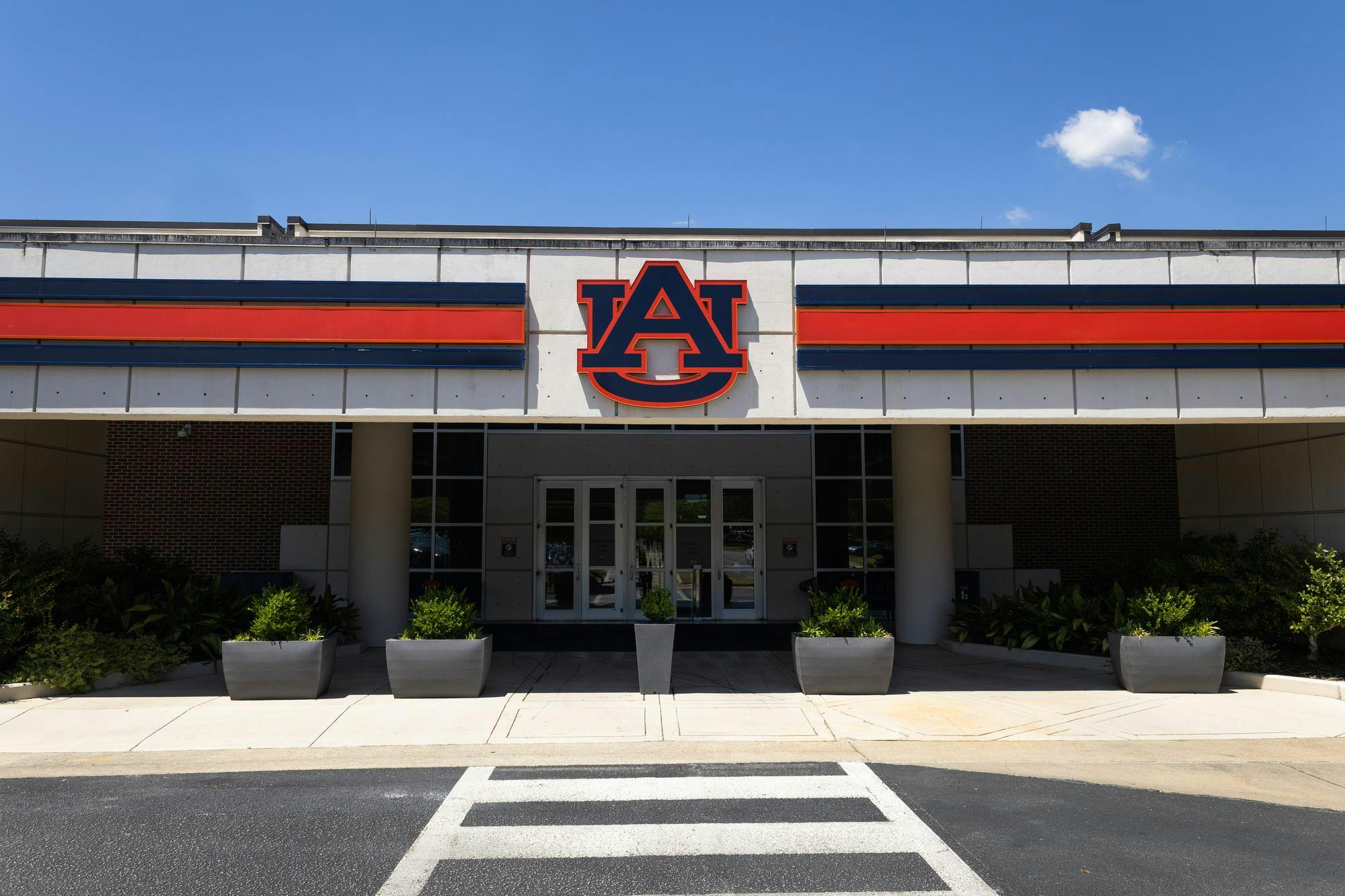 A large building entrance features a prominent orange and blue "AU" logo above glass doors, flanked by planters.