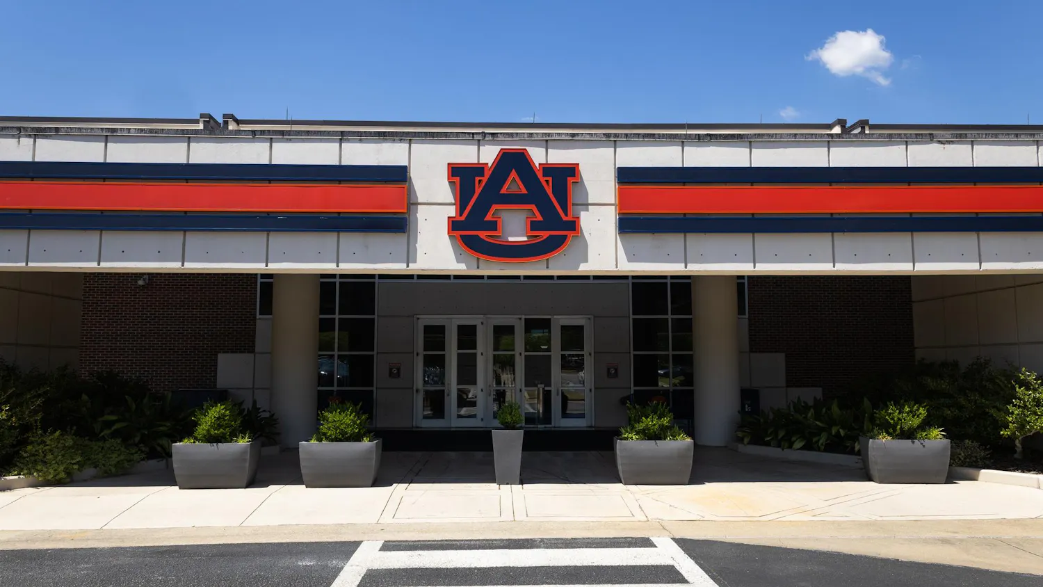 A large building entrance features a prominent orange and blue "AU" logo above glass doors, flanked by planters.