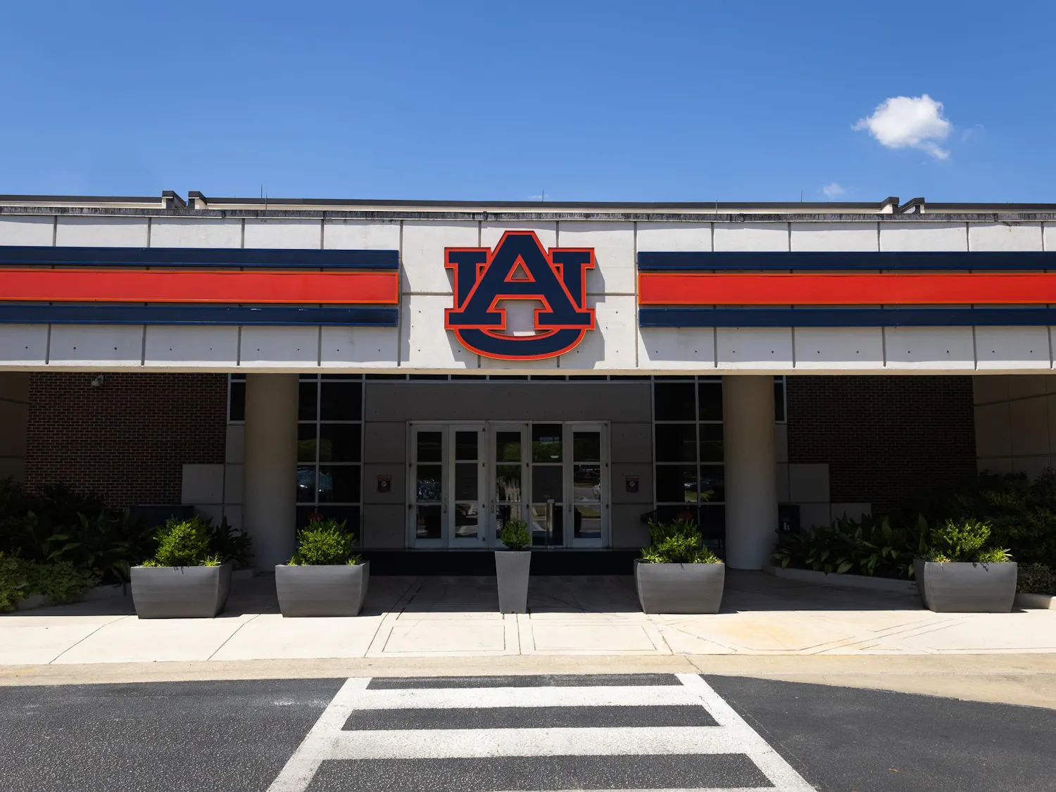 A large building entrance features a prominent orange and blue "AU" logo above glass doors, flanked by planters.