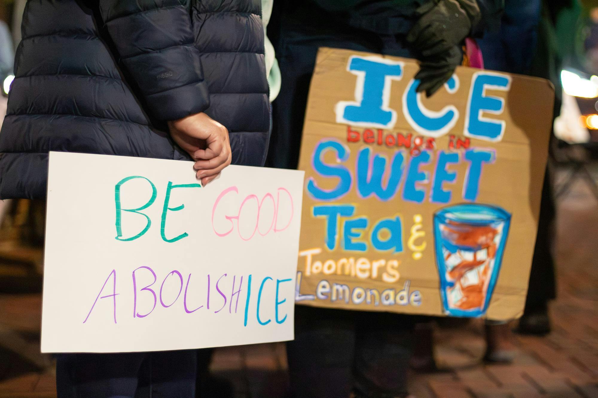 Two protestors hold signs that say "Be good, Abolish ICE" and "Ice belongs in sweet tea and Toomer's lemonade" at the protest against ICE, Immigration and Customs Enforcement, on Jan. 21, 2026 on Toomer's Corner in Auburn, Ala.