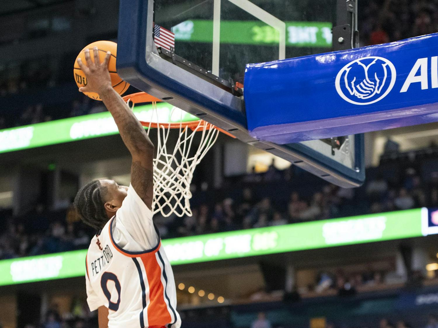 A player in a white jersey leaps to dunk a basketball into a hoop, with spectators in the background.