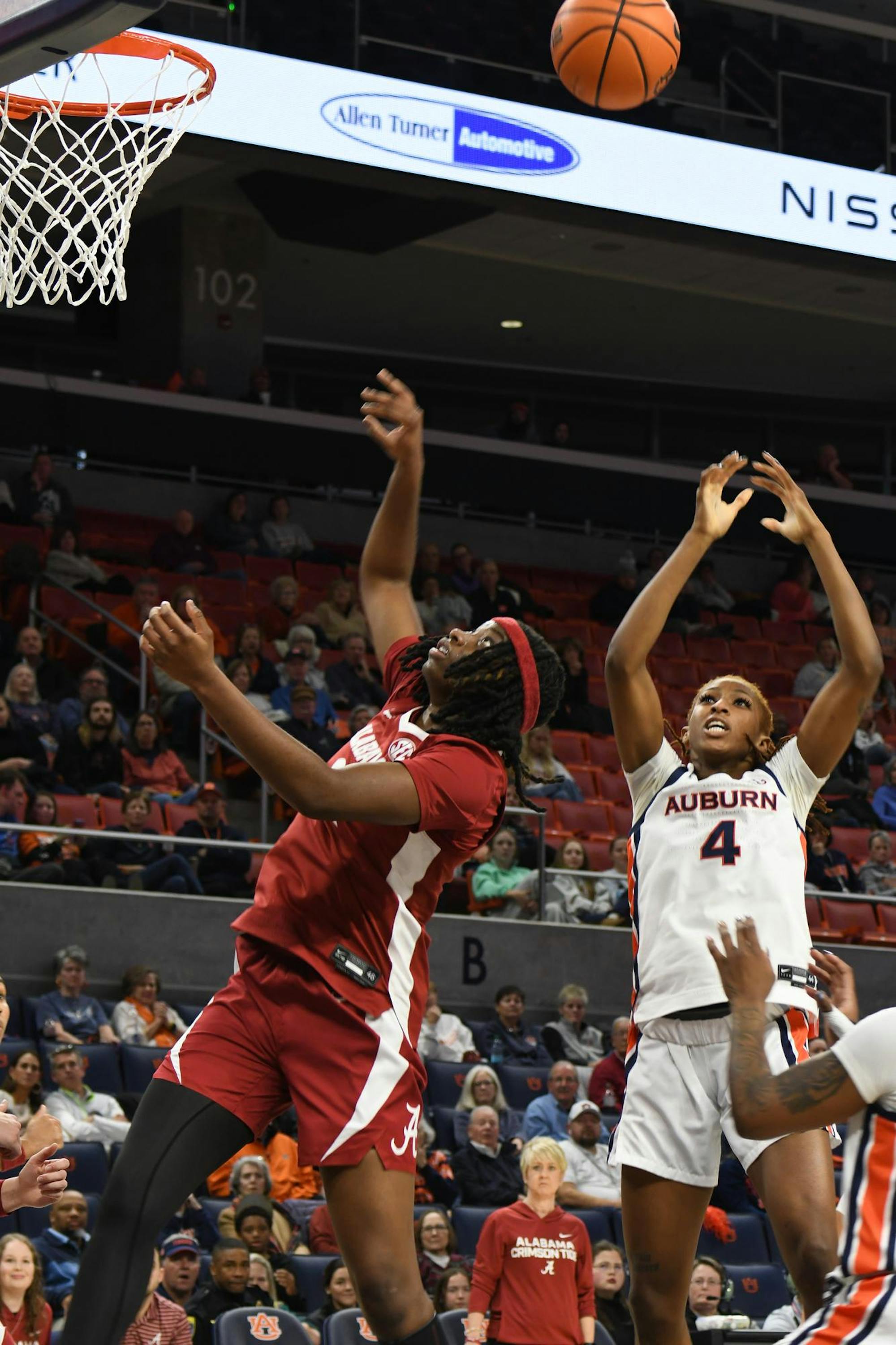 Two basketball players are competing for the ball near the hoop, with spectators watching in the background.