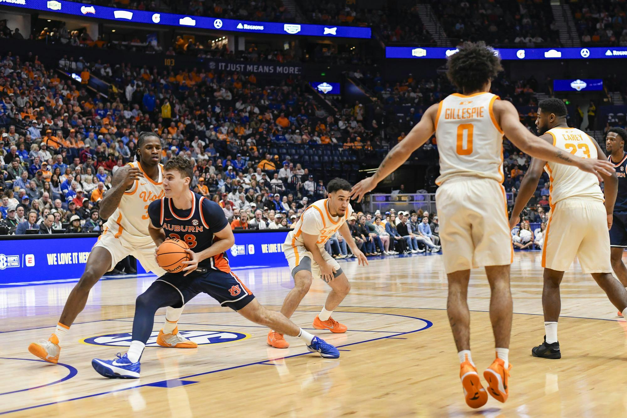 A basketball player in an orange and navy uniform is dribbling while being closely defended by an opponent in white and orange.