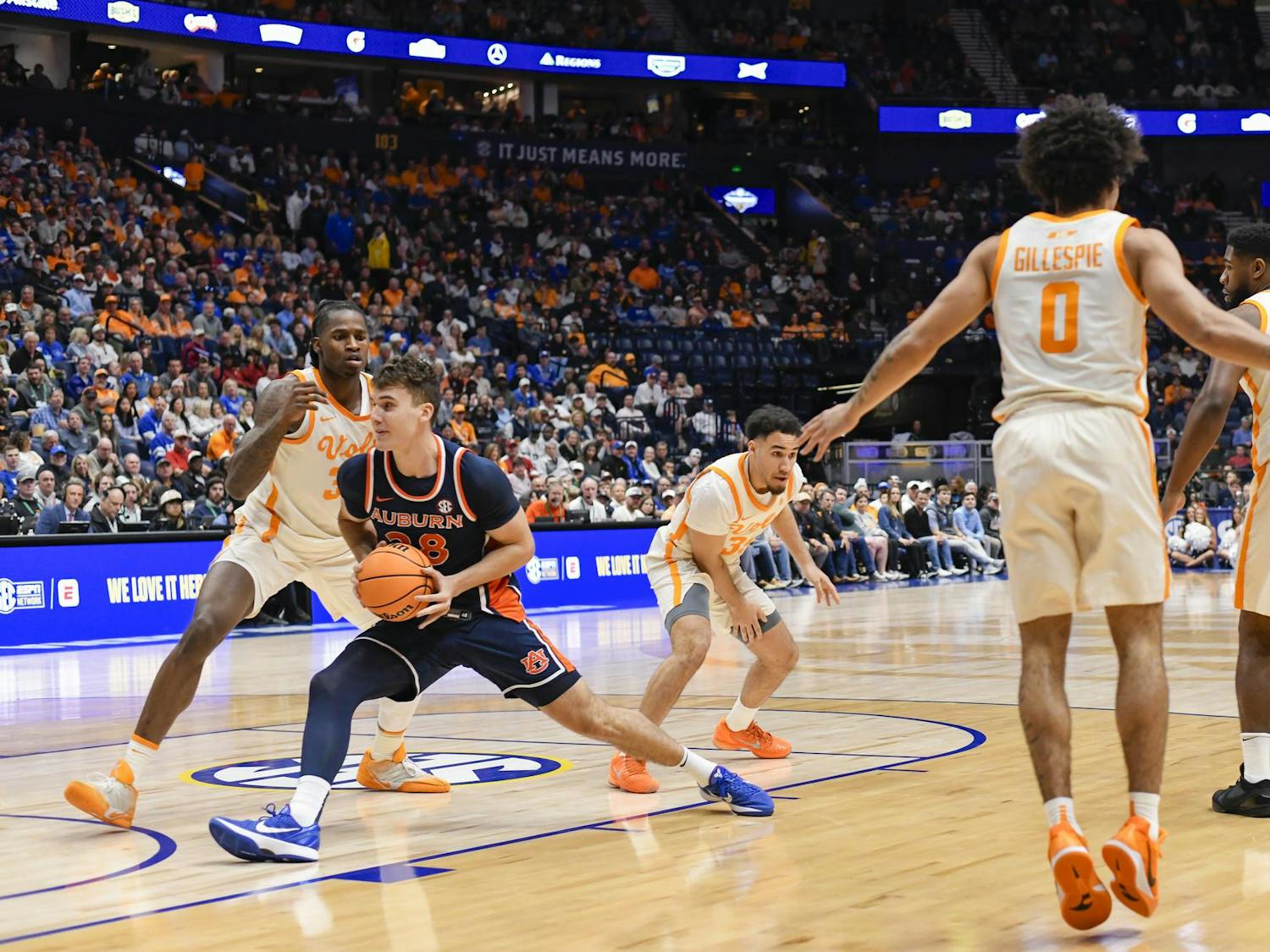 A basketball player in an orange and navy uniform is dribbling while being closely defended by an opponent in white and orange.