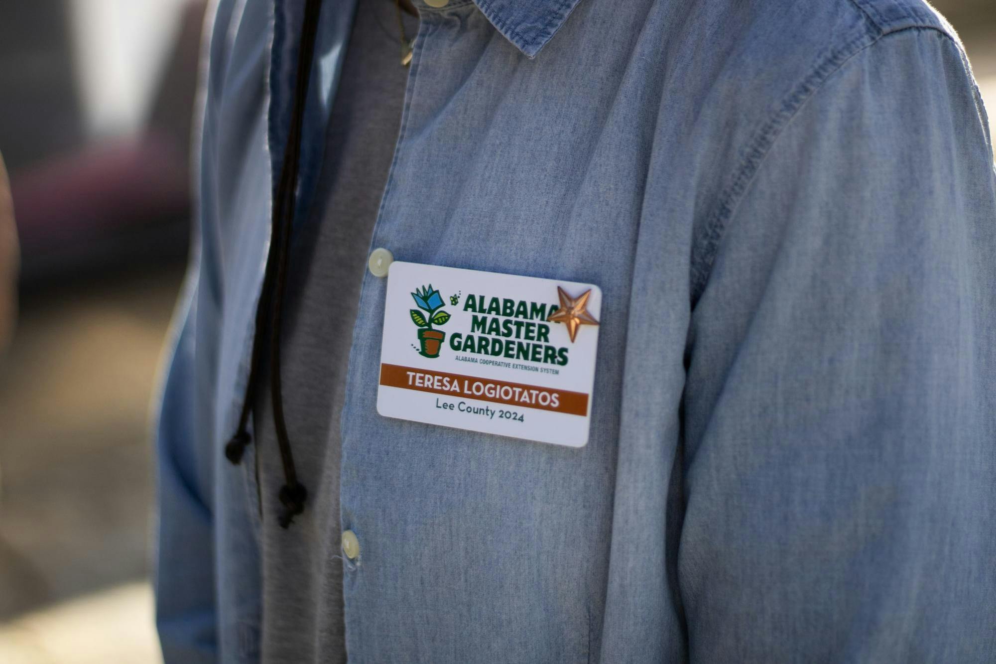 A blue shirt features a name badge that reads "ALABAMA MASTER GARDENERS," with a plant graphic, a star, and the name "TERESA LOGIOTATOS."