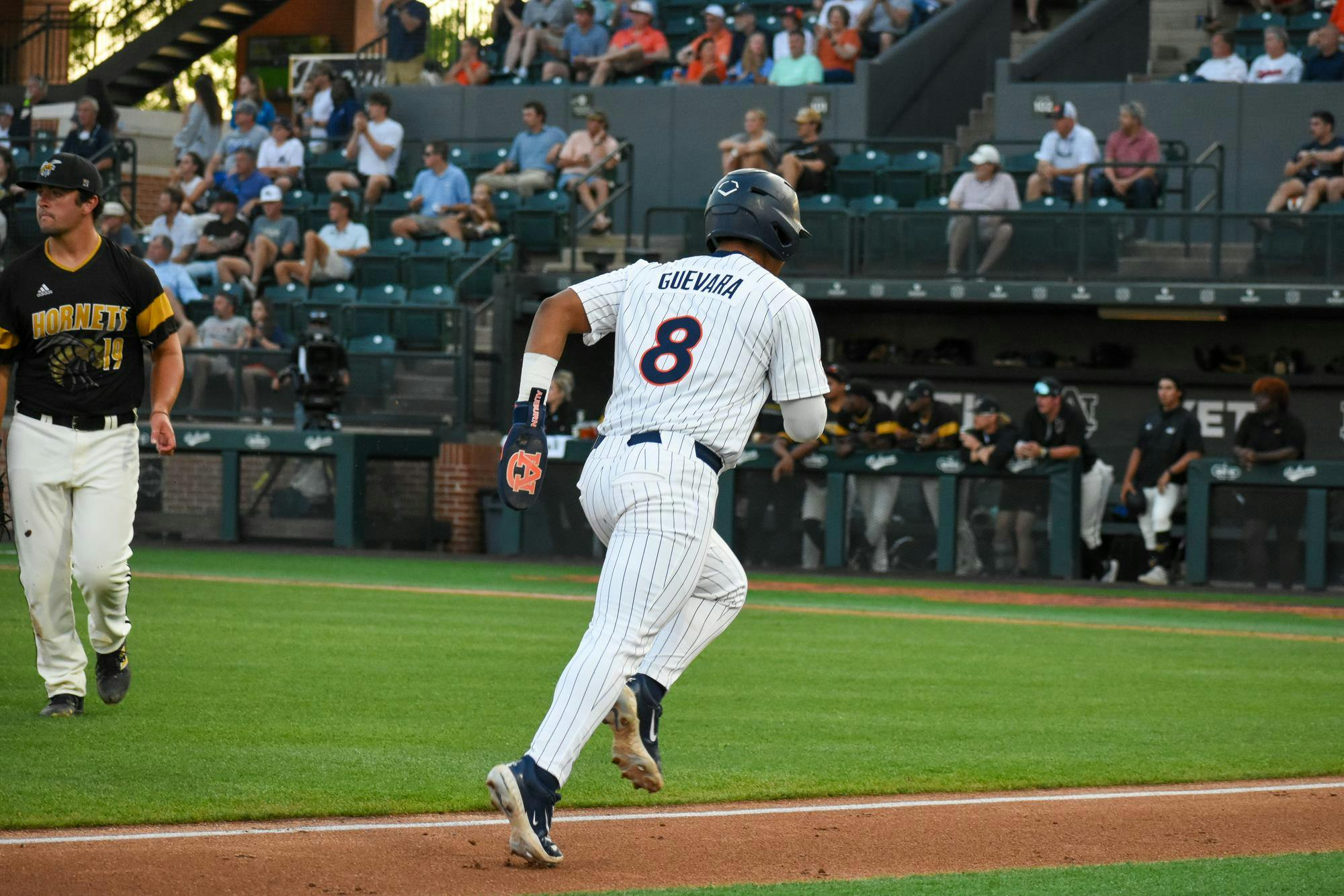 A baseball player in a white pinstriped uniform with the number 8 runs on a green field as spectators watch from the stands.