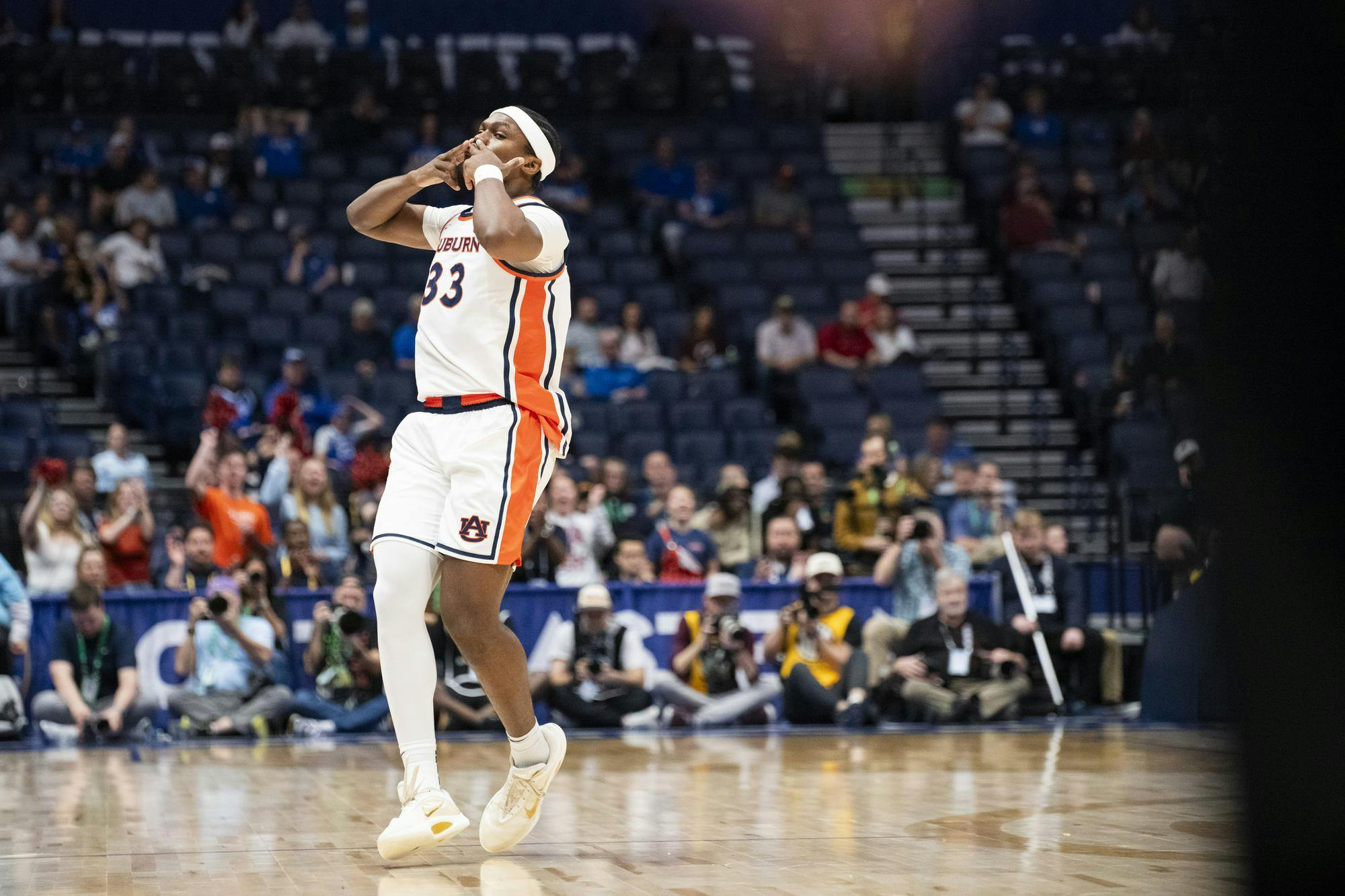 A basketball player in a white uniform with orange details celebrates enthusiastically on the court while fans cheer around him.
