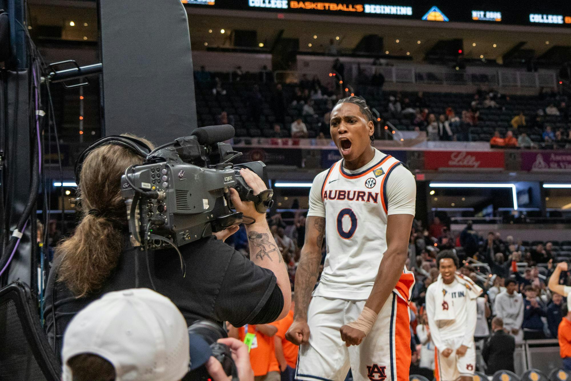 A basketball player in an Auburn jersey yells with excitement towards a camera, while teammates celebrate in the background.