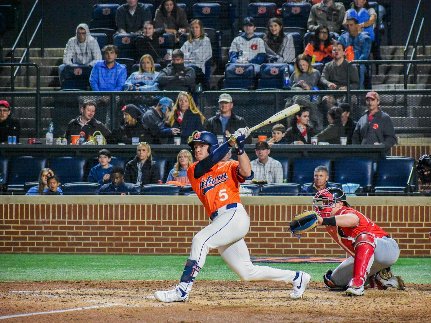 A baseball player swings a bat as a catcher crouches behind him, surrounded by a crowd in the stands.