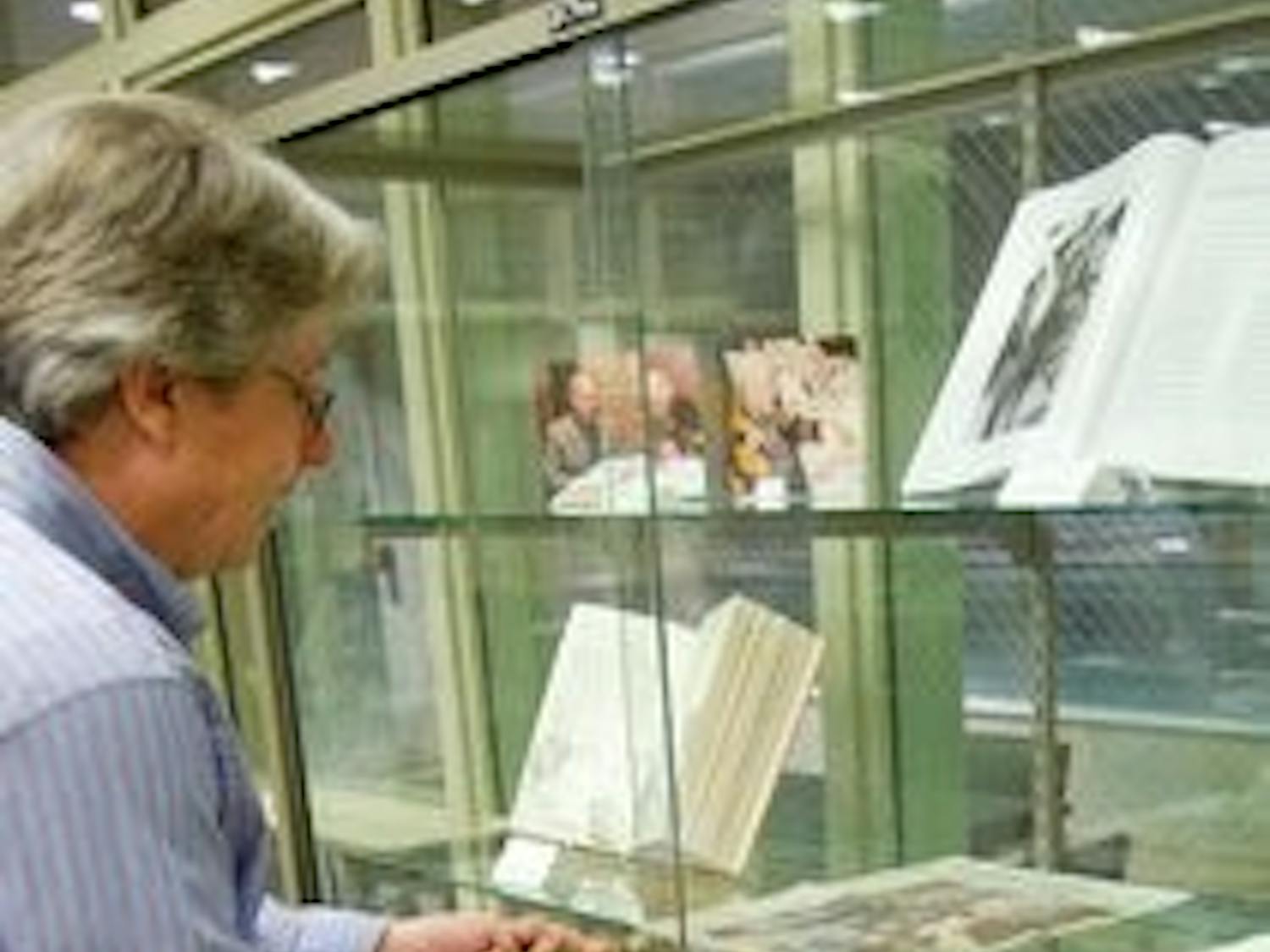 John Varner, a University Archives employee, opens the display case to turn "Jeffrey's Latest 13 More Alabama Ghosts" book to the story about the Auburn Spirit. (Kristen Ferrell / CAMPUS EDITOR)