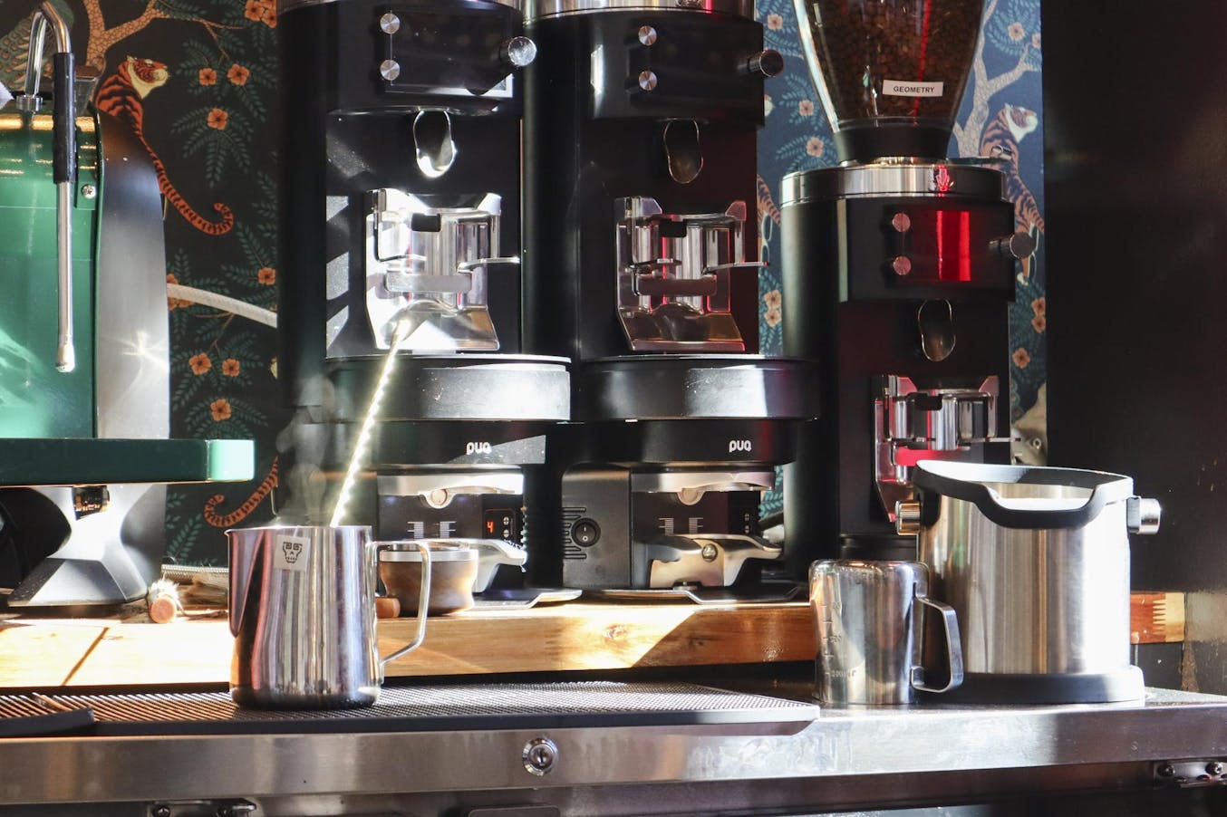 Several coffee machines are arranged on a countertop, with steaming milk frothing in a metallic pitcher beside them.