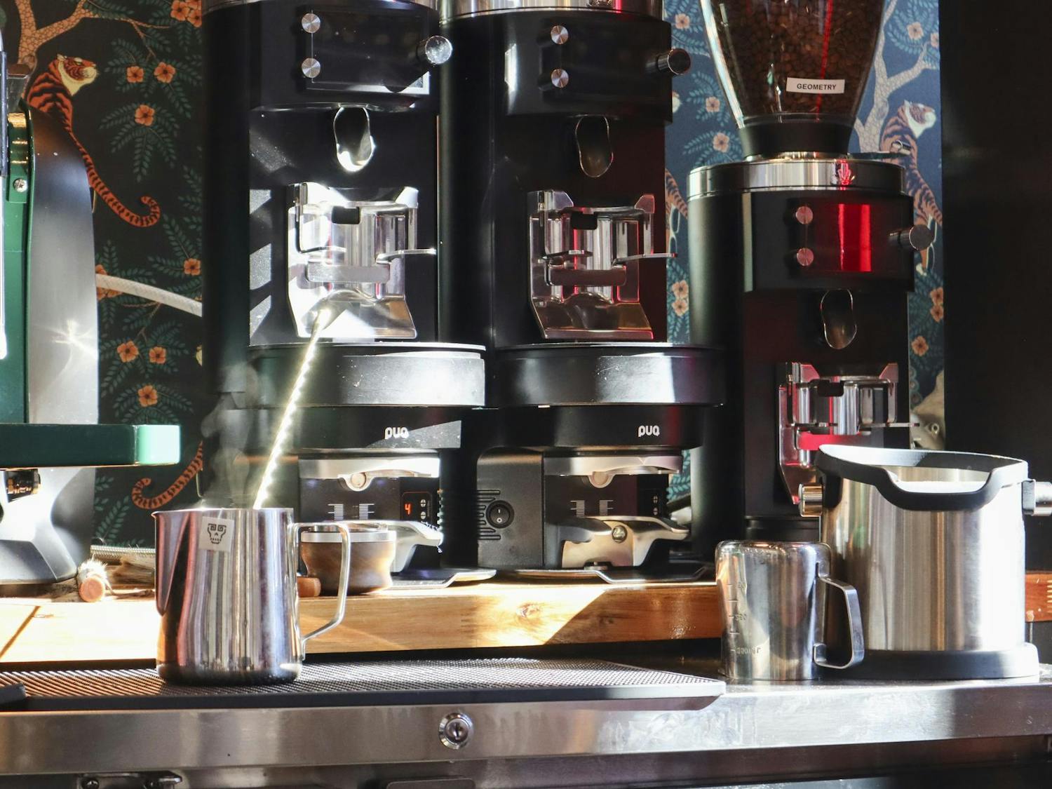 Several coffee machines are arranged on a countertop, with steaming milk frothing in a metallic pitcher beside them.