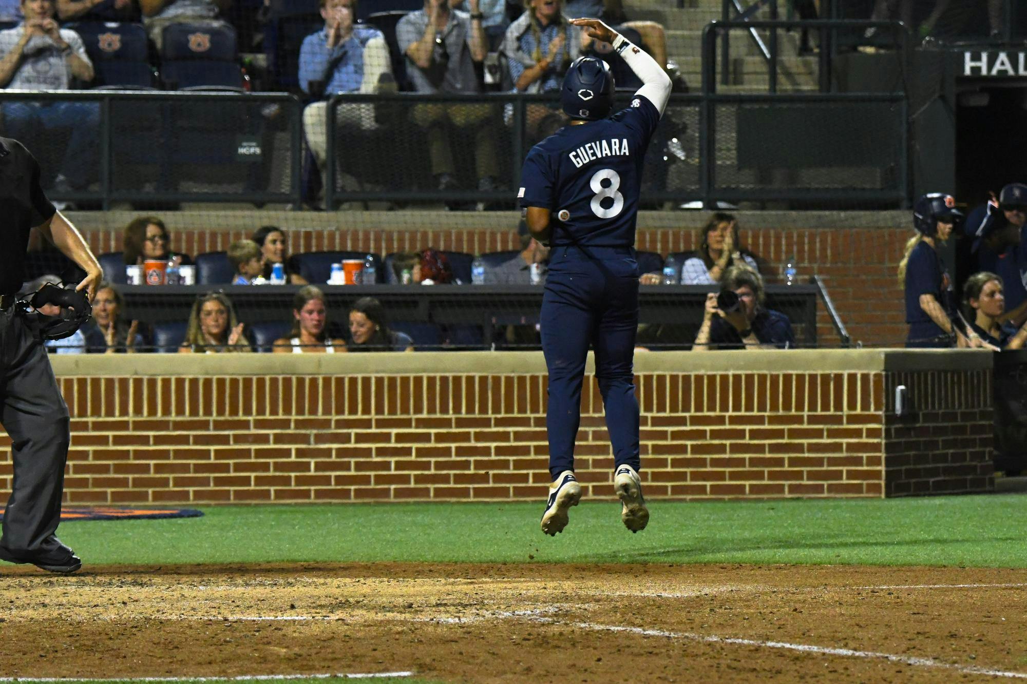 A baseball player wearing a blue uniform and number 8 is jumping, while spectators in the background are applauding.