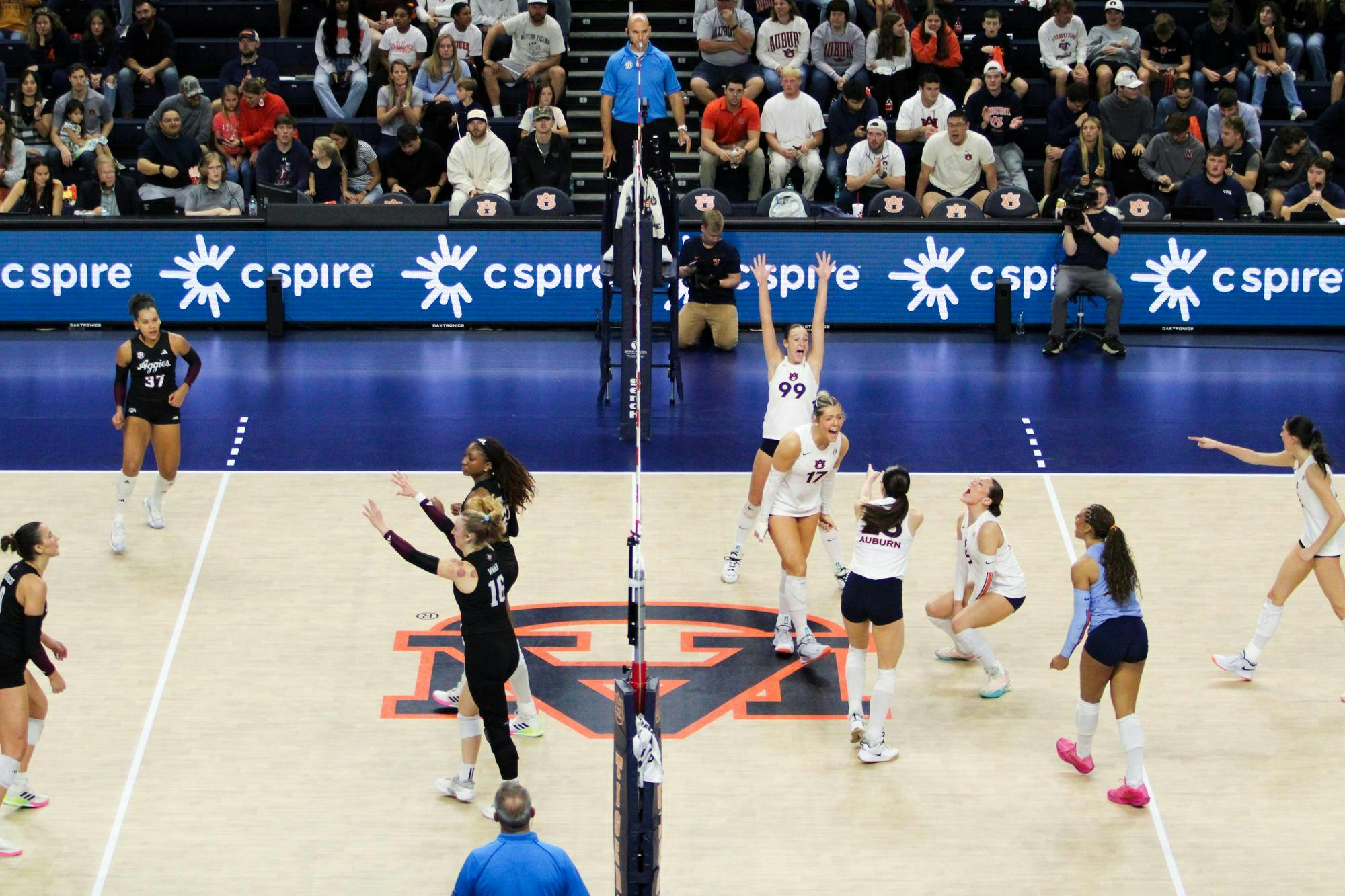 A volleyball match is in progress with players from two teams positioned on opposite sides of the net.