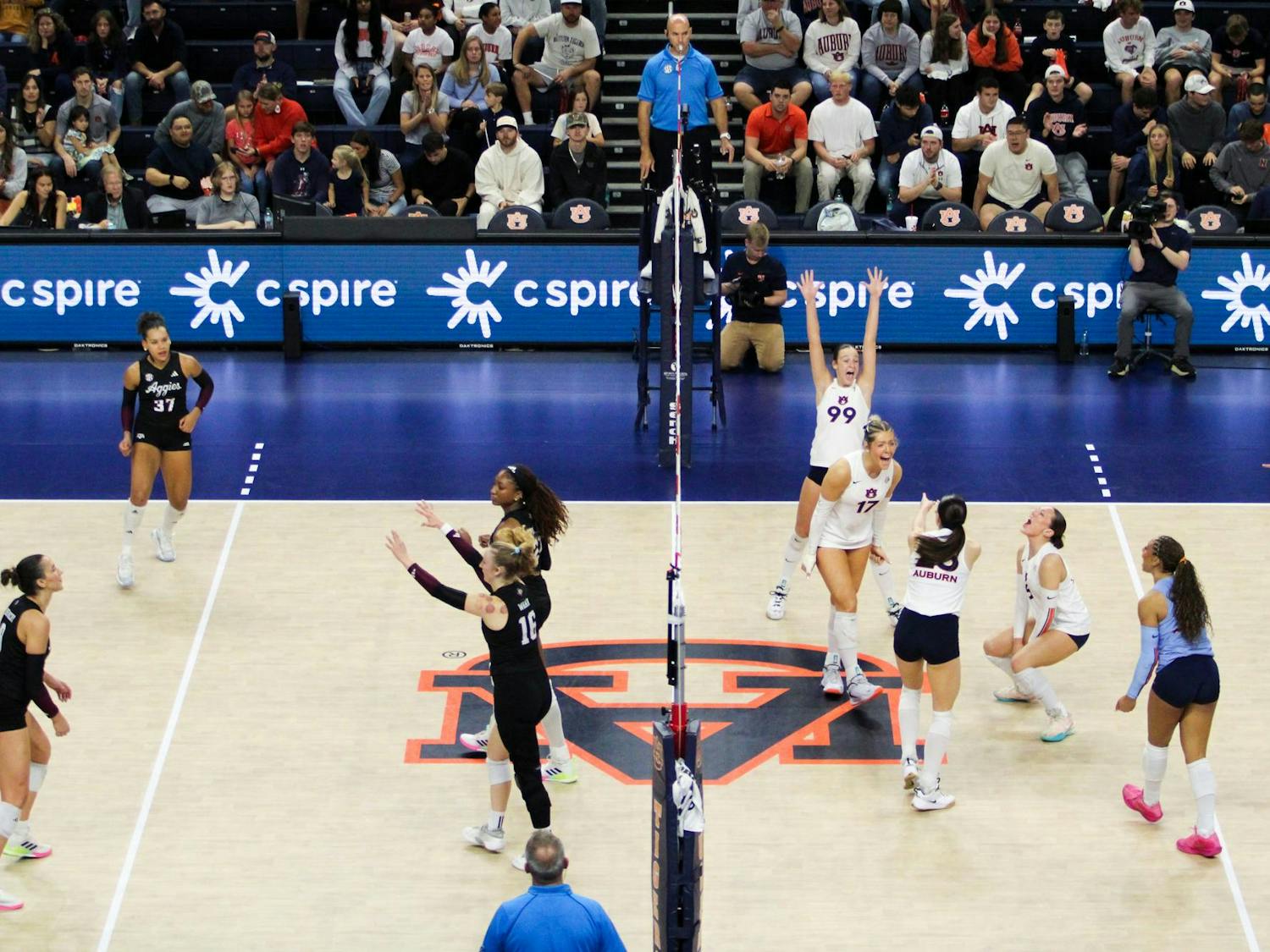 A volleyball match is in progress with players from two teams positioned on opposite sides of the net.